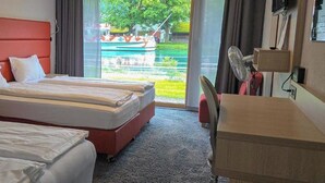 A hotel room with two beds, a desk, and a view of a body of water and greenery outside. - The River Village (Interlaken)