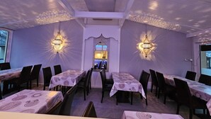 An indoor dining area with tables and chairs, decorative wall sconces, and a view through a window. - The River Village (Interlaken)