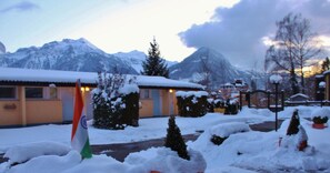 A building with a snow-covered roof, a flag, and a mountainous backdrop. - The River Village (Interlaken)