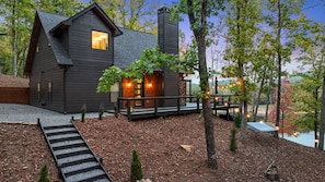 A cabin with a deck, a chimney, and a view of a lake.