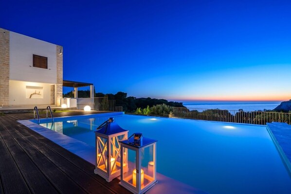 Una piscina moderna al aire libre con vista al mar al atardecer.