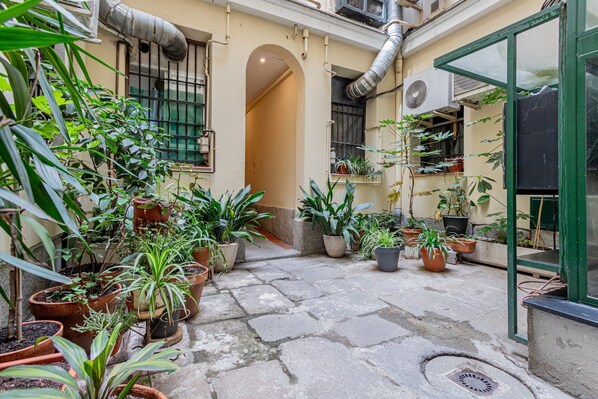 Un patio con plantas en macetas, suelo de piedra y un edificio con un equipo de aire acondicionado.
