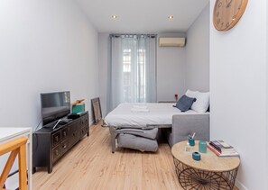 Ein modernes Hotelzimmer mit einem Bett, einem Fernseher, einem Schreibtisch und einem kleinen runden Tisch mit Büchern und einer Lampe.