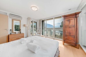 Ein Schlafzimmer mit einem großen Bett, einem Holzschrank, einem Spiegel, einem Nachttisch und Blick ins Freie.