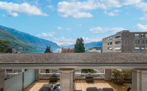 Eine Terrasse mit Blick auf einen See und Berge, ein Gebäude mit modernem Design und einem klaren Himmel.