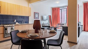 Een moderne keuken met houten kasten, een eethoek met een ronde tafel en zwarte stoelen, en een zithoek met een bank en rode gordijnen.
