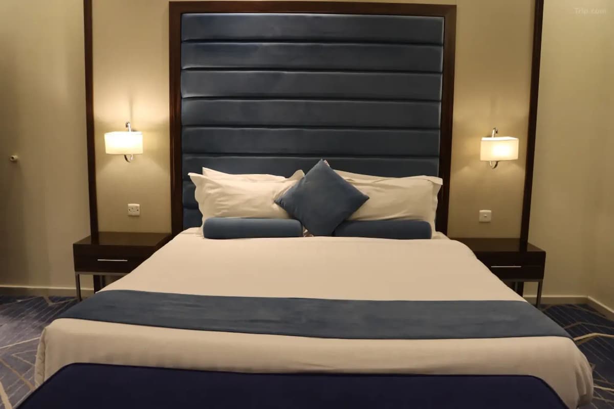 A hotel room with a large bed, two bedside tables, and wall-mounted lamps.