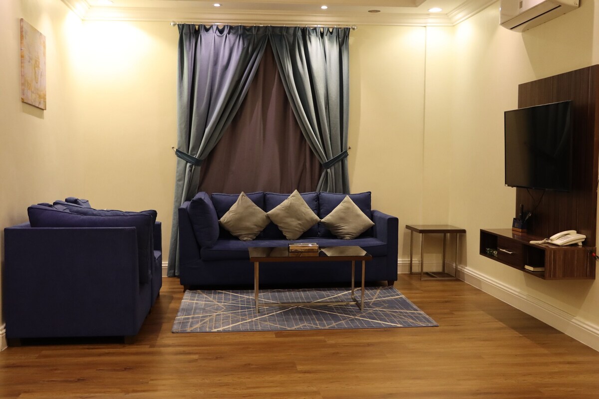 A living room with a sofa, a small table, a TV, and a wall-mounted phone.