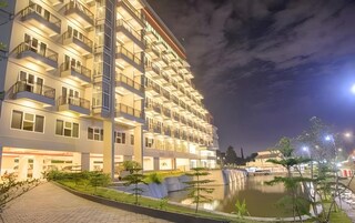 Un hotel de varios pisos con balcones, una fuente de agua y un paseo pavimentado.