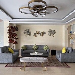 Ein stilvolles Wohnzimmer mit einem grauen Sofagarnitur, einem weißen Hocker und Wanddekoration.