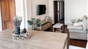 A modern living room with a wooden dining table, a sofa, a TV, and a staircase. - Lujoso amplio dpto para 8 en Salta con cochera (Salta)