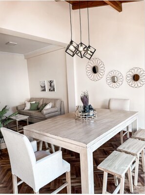 A dining area with a wooden table, white chairs, and a hanging light fixture. - Lujoso amplio dpto para 8 en Salta con cochera (Salta)