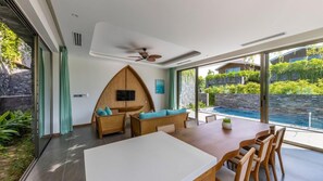 A modern interior with a dining area, a ceiling fan, and a view of a pool and greenery outside. - Bellerive Hoi An Resort & Spa (Da Nang Municipality)