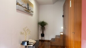 Un couloir avec un escalier, une plante en pot, un arbre décoratif et un tableau accroché au mur.