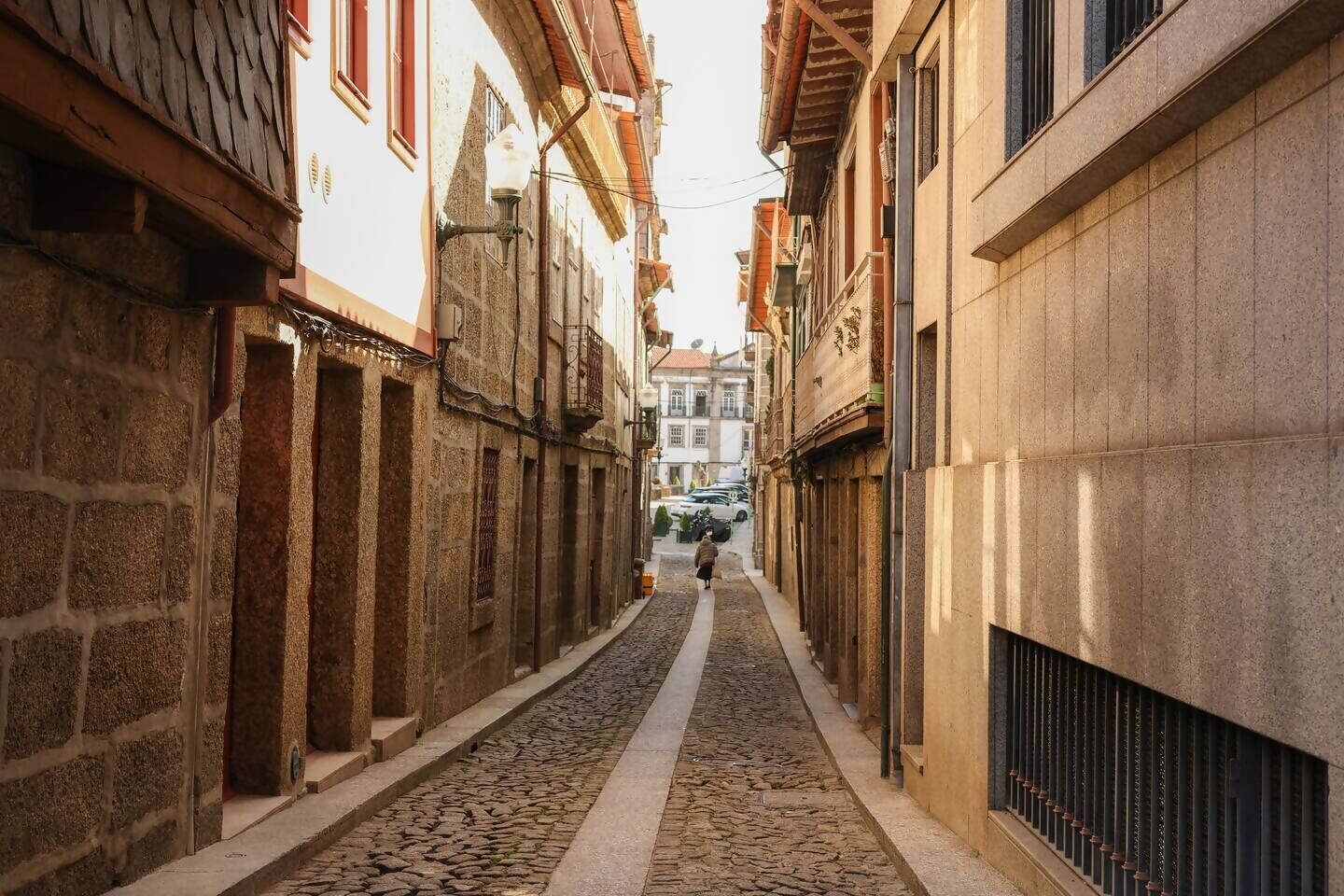 Une ruelle étroite pavée, bordée de bâtiments historiques aux façades en pierre et aux balcons traditionnels.