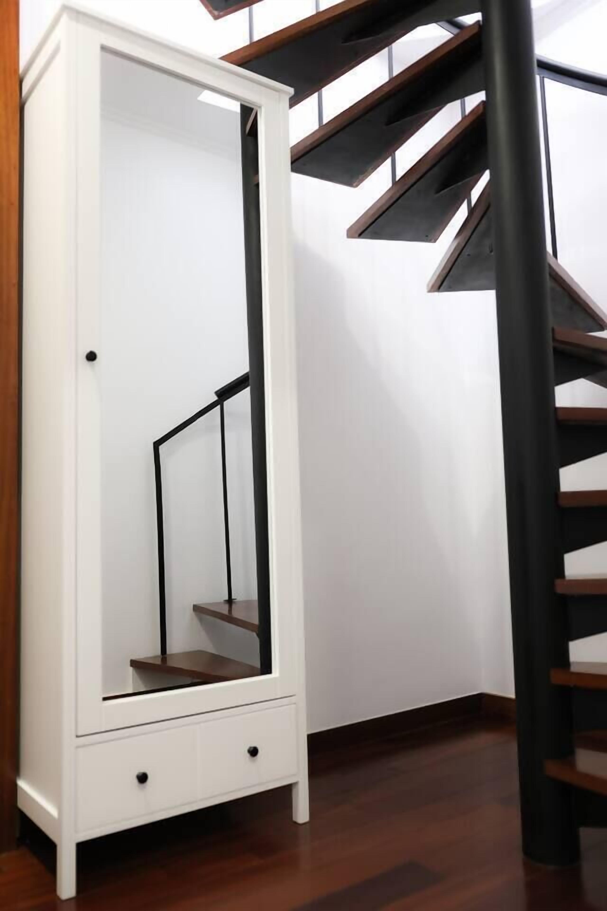 Ein weißer Kleiderschrank mit Spiegel, eine Holztreppe und eine schwarze Säule.