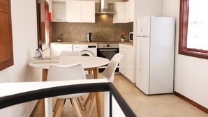 Cozinha compacta com armários brancos, forno embutido, geladeira e área de jantar com mesa e cadeiras.