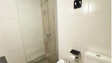 Ein kleines Badezimmer mit Dusche, Bidet, Toilette und Mülleimer.