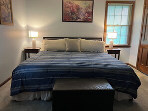 Ein Schlafzimmer mit einem Bett, zwei Nachttischen, einer Bank, einem Fenster mit Jalousien und einem Bild an der Wand.