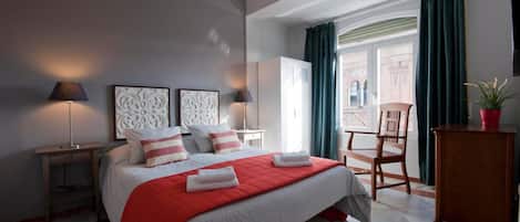 A hotel room with a bed, two bedside tables, a chair, a desk, a window with curtains, and a view of the outside.