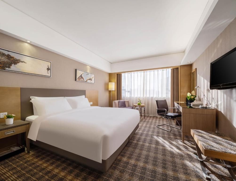 Una habitación de hotel con una cama grande, un escritorio, una silla, un televisor y obras de arte en las paredes.