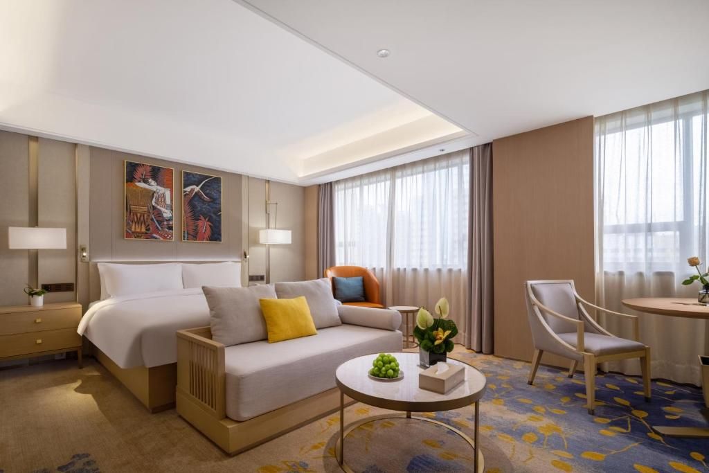 Una habitación de hotel con una cama, un sofá, una mesa de centro, una silla, una lámpara y un cuadro en la pared.