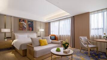 Una habitación de hotel con una cama, un sofá, una mesa de centro, una silla, una lámpara y un cuadro en la pared.