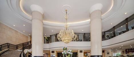 A spacious lobby with a grand chandelier, a staircase, and a reception desk.
