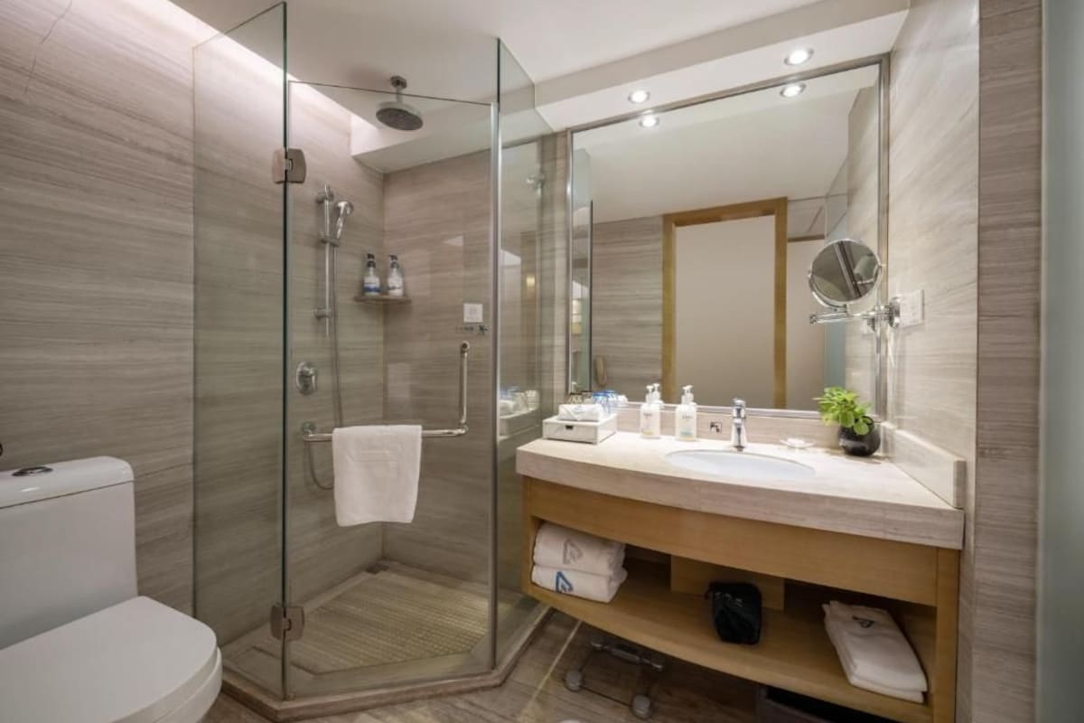 A modern bathroom with a glass-enclosed shower, a large mirror, and a vanity with a sink and storage.