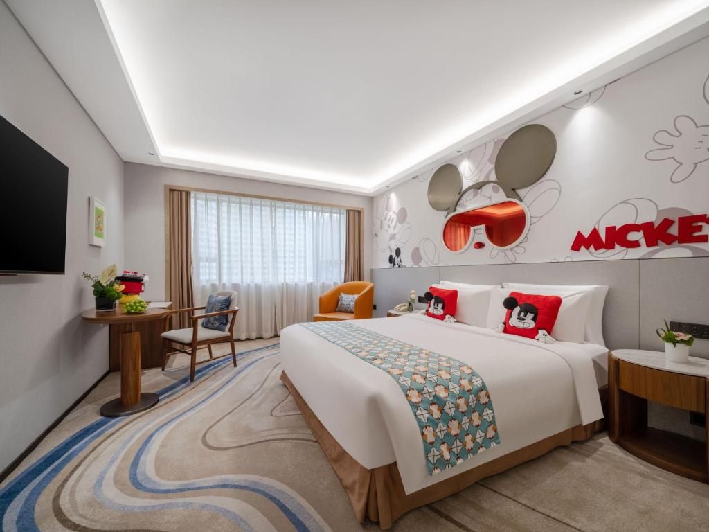 A hotel room with a bed, a desk, a chair, a TV, and Mickey Mouse-themed decor.