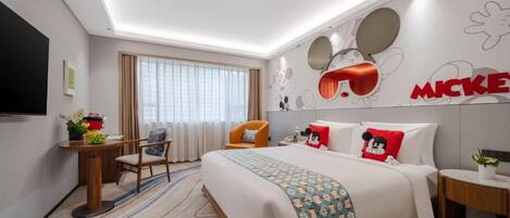 A hotel room with a bed, a desk, a chair, a TV, and Mickey Mouse-themed decor.