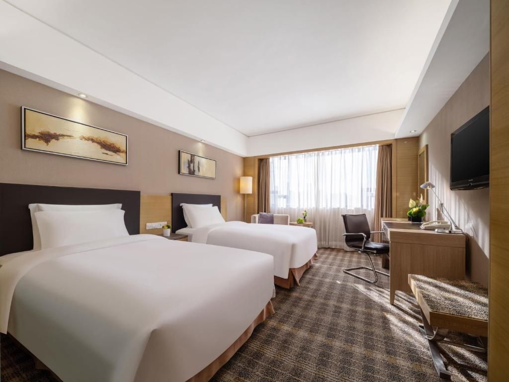 A hotel room with two beds, a desk, a chair, a TV, and artwork on the walls.