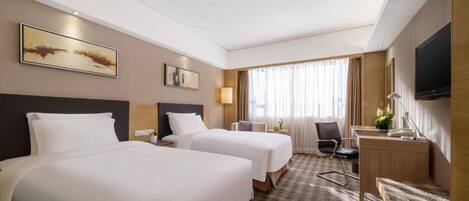 A hotel room with two beds, a desk, a chair, a TV, and artwork on the walls.