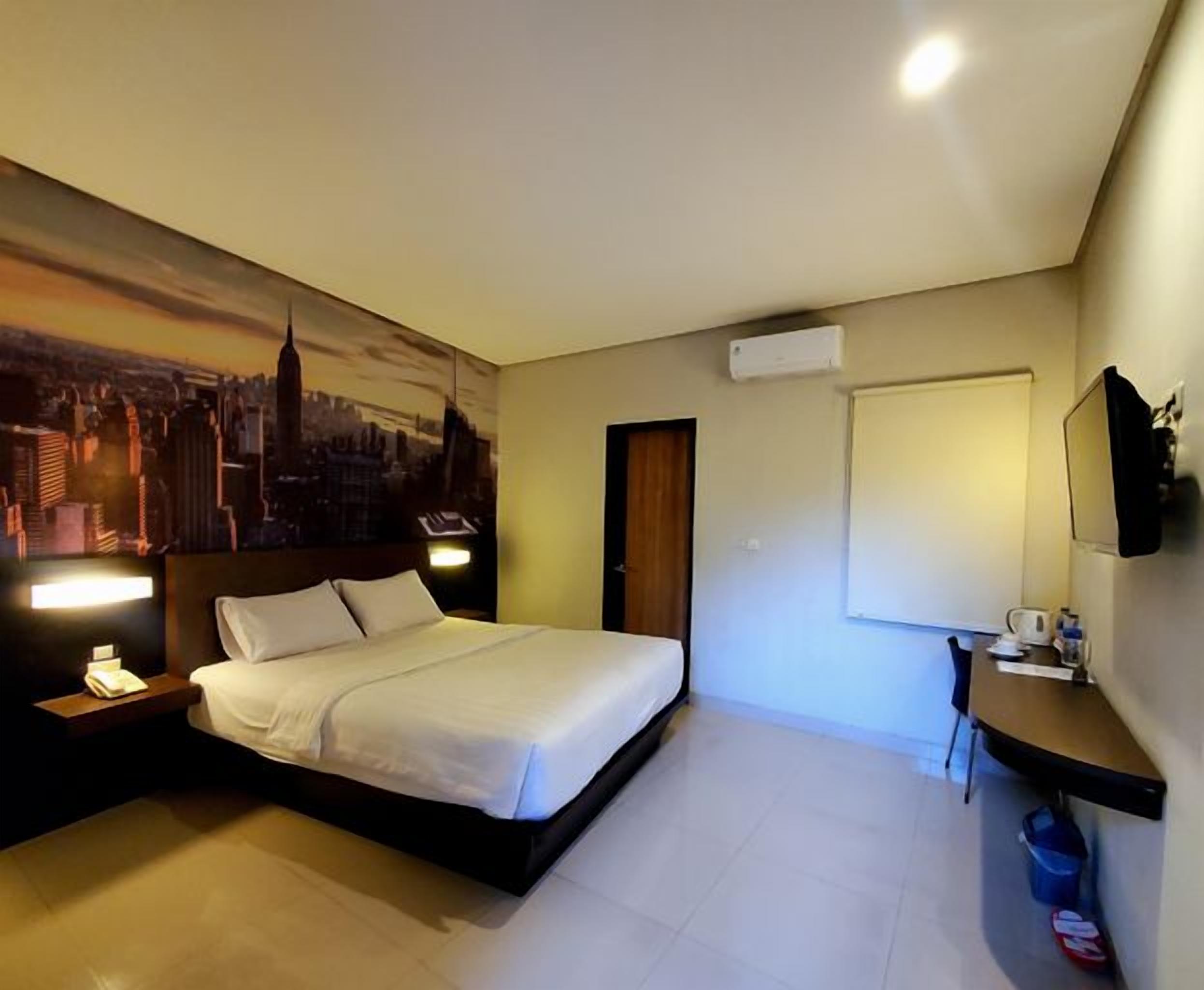 A hotel room with a bed, bedside table, lamp, and a cityscape mural on the wall.
