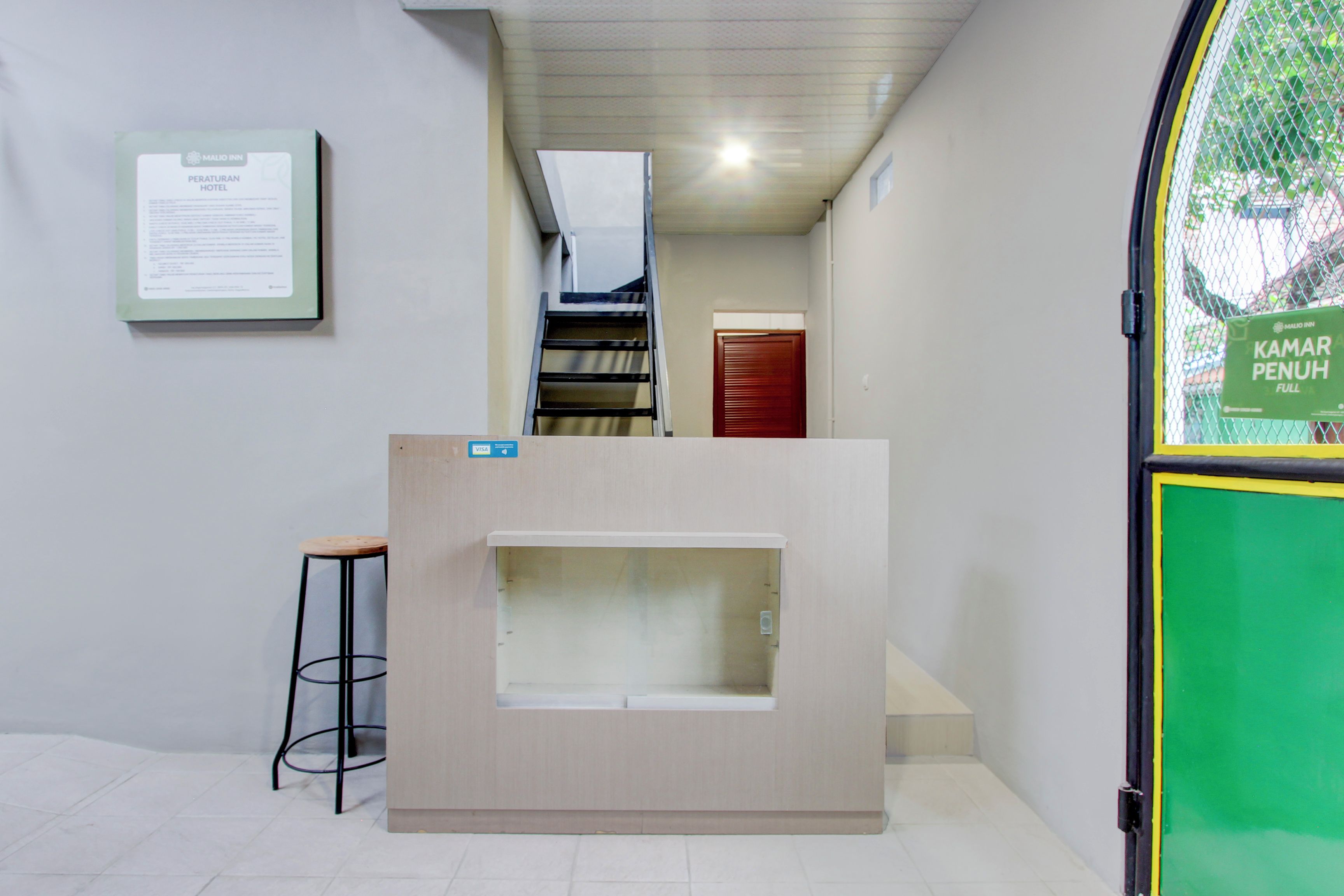 A reception desk with a staircase leading to an upper level, a framed notice on the wall, and a green sign on the door.