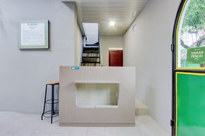 Ein Empfangsschalter mit einer Treppe, die zu einer oberen Ebene führt, ein gerahmtes Aushang an der Wand und ein grünes Schild an der Tür.