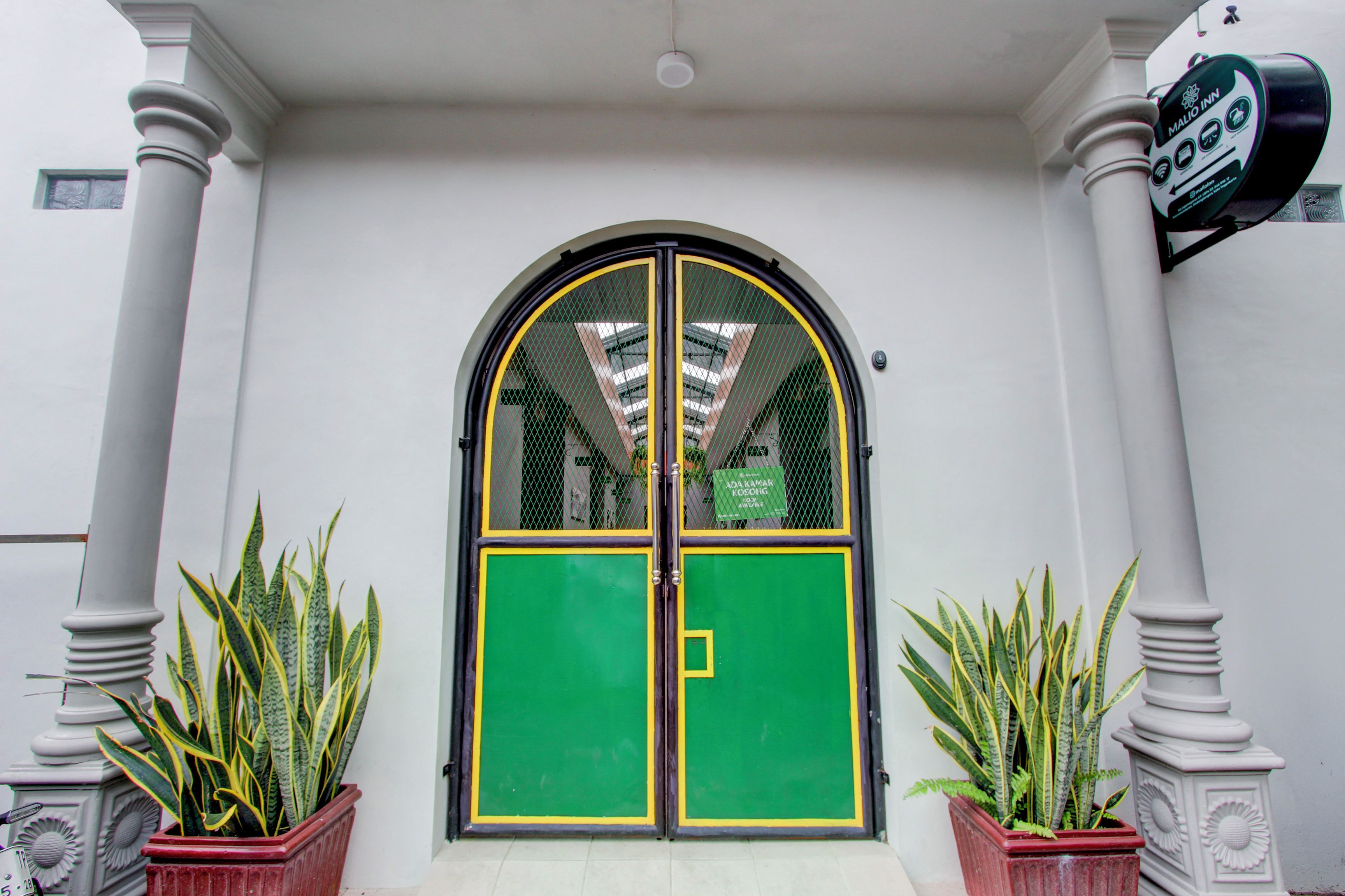 A building entrance with a green and yellow door, flanked by white columns and potted plants.