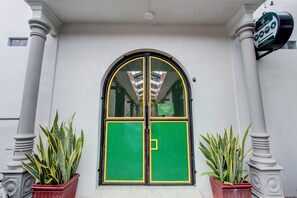 A building entrance with a green and yellow door, flanked by white columns and potted plants. - Hotel O Yogyakarta Near Jalan Malioboro (Yogyakarta)