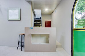 Una recepción con una escalera que lleva a un nivel superior, un aviso enmarcado en la pared y un cartel verde en la puerta.
