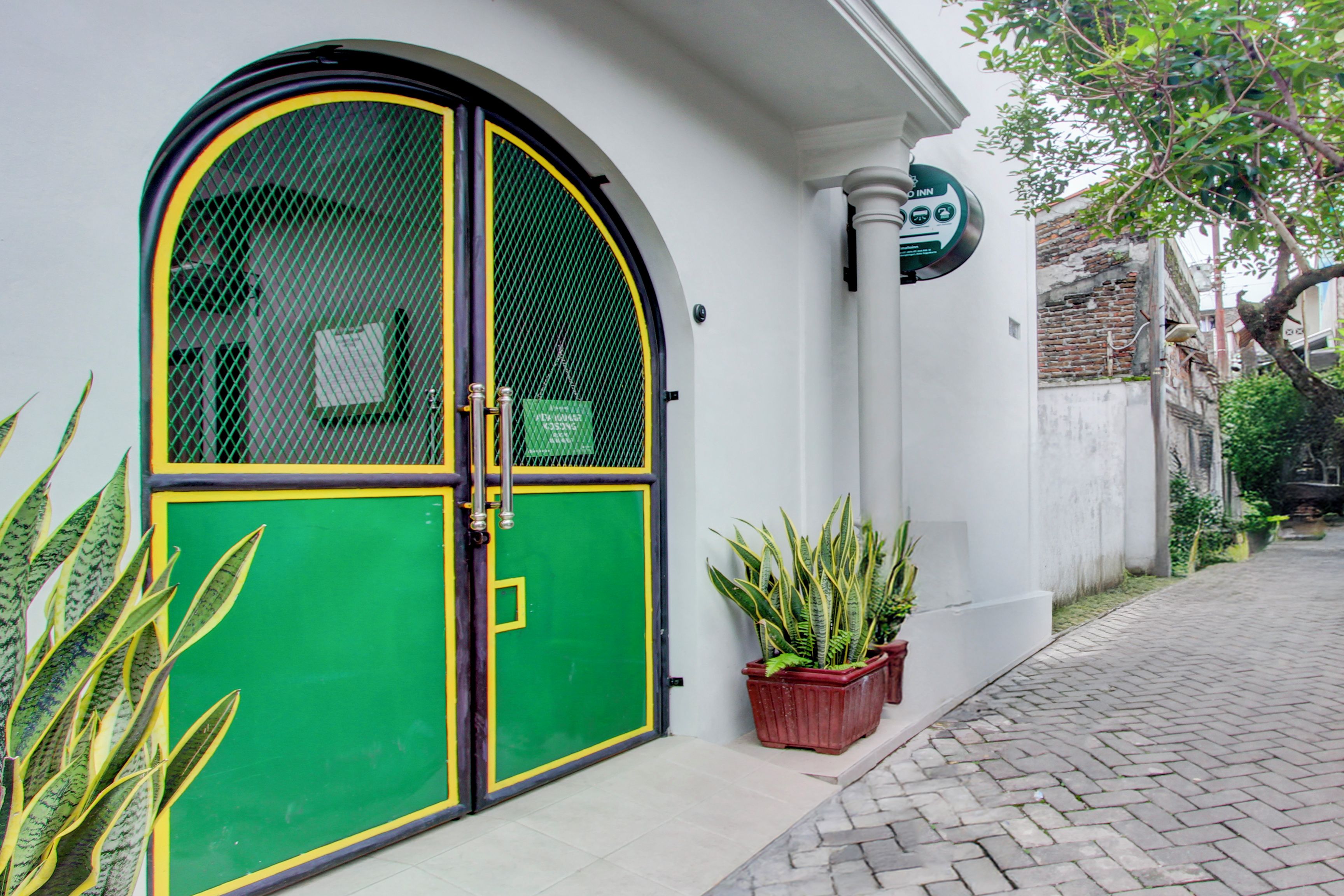 Un bâtiment avec une porte verte et jaune, des plantes en pot et une enseigne indiquant qu’il s’agit d’un hôtel.