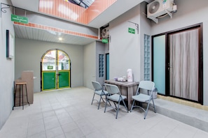 Un área de espera con una mesa y sillas, un taburete, un ventilador y una puerta verde que dice "MALO DELUXE".