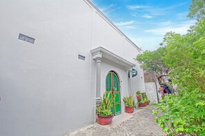 A narrow cobblestone street with a white building featuring a green door and potted plants. - Hotel O Yogyakarta Near Jalan Malioboro (Yogyakarta)