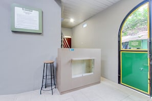 Una recepción con un cartel, un taburete y una puerta verde con marco amarillo.