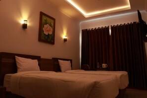 Habitació d'hotel amb un llit doble, dues taules de nit, una tauleta auxiliar, un quadre a la paret i una finestra amb cortines.