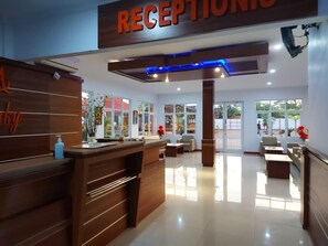 Una zona d'entrada amb una taula de recepció de fusta, un cartell a sobre i una zona d'estar amb un sofà i cadires.