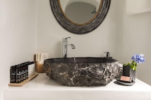 A bathroom with a stone sink, a mirror, and toiletries. - Summer Lovers Villa (Santorini)