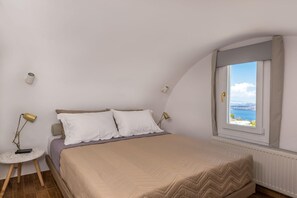 Quarto com uma cama, duas luminárias de cabeceira, uma mesa redonda, uma janela com vista e um radiador.