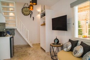 Uma sala de estar moderna com televisão, almofadas decorativas, um relógio e uma escada que leva a uma cozinha.
