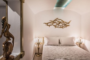 A bedroom with a bed, two bedside lamps, a wall-mounted decor piece, and a sculpture. - Summer Lovers Villa (Santorini)