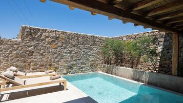 Una piscina con sillones de descanso, un muro de piedra y una pérgola de madera.